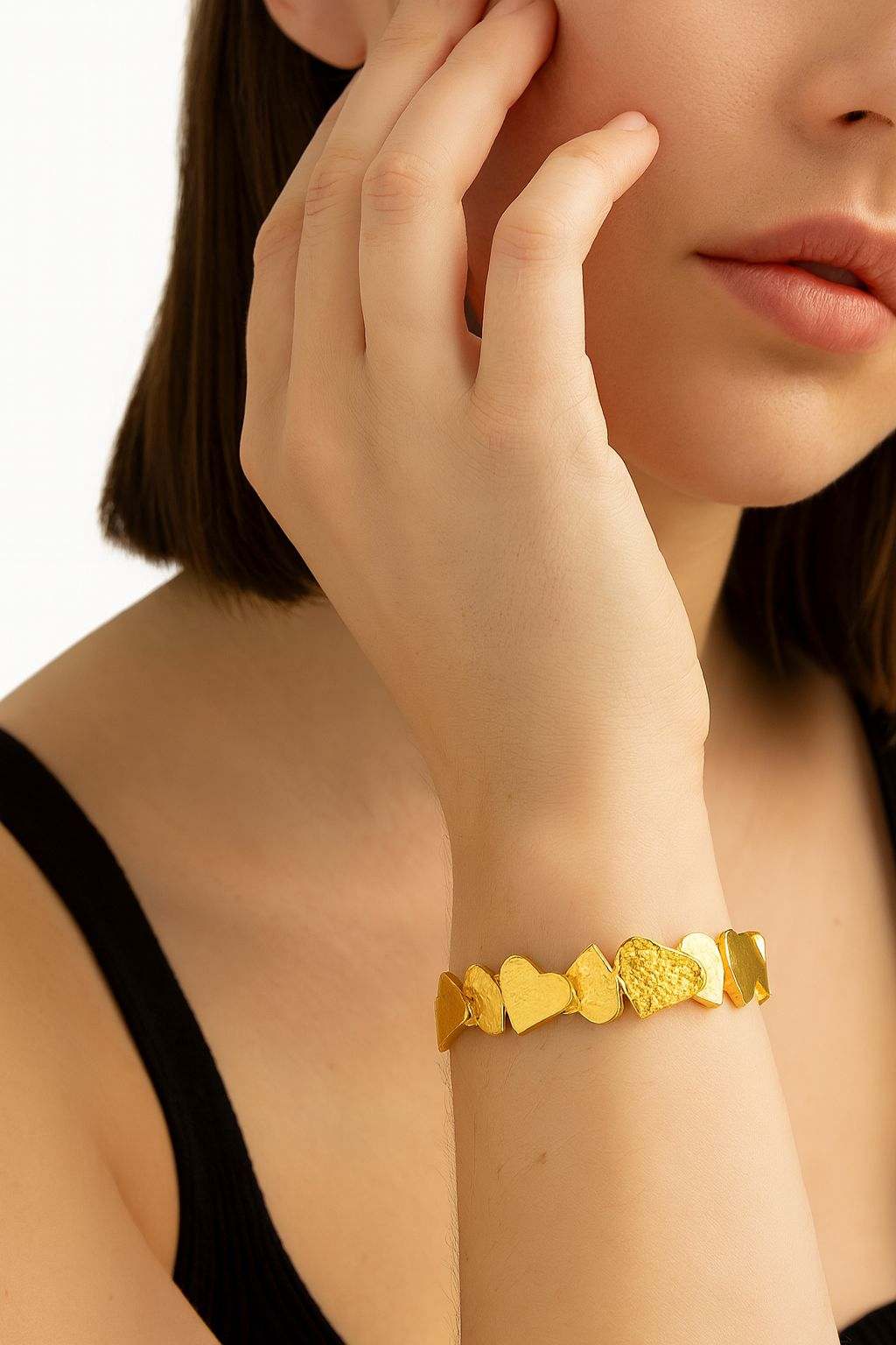 Close-up of a woman's wrist wearing a textured heart gold bracelet with layered heart charms and a hand-painted finish.