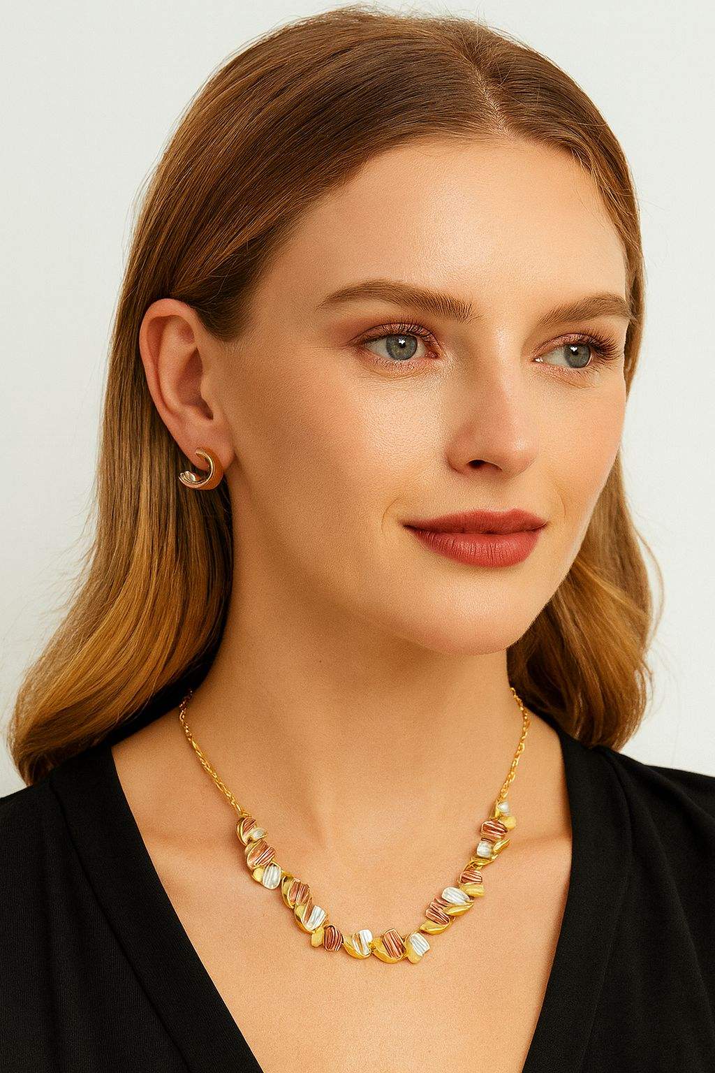 Woman wearing elegant gold necklace set with matching earrings in tricolor wave design