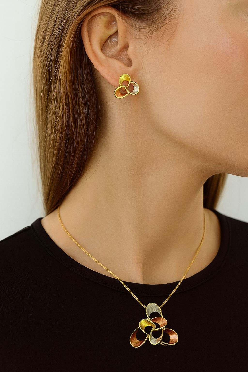 Elegant geometric gold pendant necklace and stud earrings set with tricolor design worn by woman